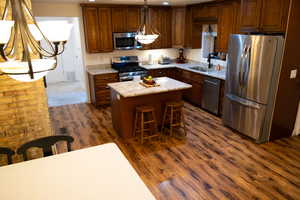 Kitchen featuring hanging light fixtures, stainless steel appliances, a center island, light stone countertops, and sink