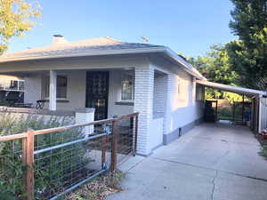 View of front of home featuring brick siding, a porch, concrete driveway, fence, and an attached carport