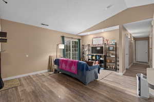 Living area with visible vents, vaulted ceiling, baseboards, and wood finished floors