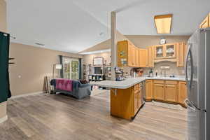 Kitchen with glass insert cabinets, appliances with stainless steel finishes, open floor plan, a peninsula, and light countertops