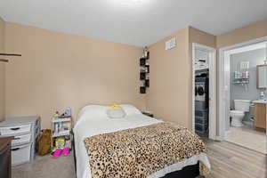 Bedroom featuring visible vents, a textured ceiling, ensuite bath, and light wood finished floors