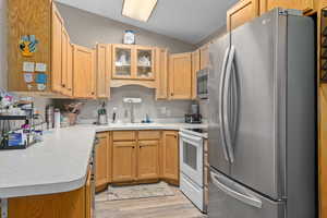 Kitchen featuring lofted ceiling, a sink, light countertops, appliances with stainless steel finishes, and glass insert cabinets