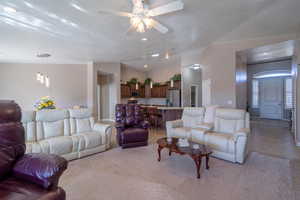 Living area featuring light tile patterned floors, lofted ceiling, light carpet, ceiling fan, and a textured ceiling