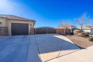 View of front of property featuring driveway, stone siding, a gate, and stucco siding