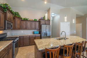 Kitchen with appliances with stainless steel finishes, a sink, an island with sink, and a kitchen bar