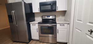 Kitchen featuring light stone countertops, light wood-style flooring, appliances with stainless steel finishes, and white cabinets