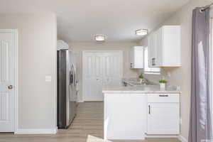 Kitchen featuring light countertops, light wood-style flooring, white cabinetry, a sink, and stainless steel fridge