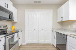 Kitchen with black appliances, white cabinetry, visible vents, and light wood-style flooring