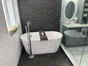 Bathroom with a freestanding tub, tile walls, vanity, and tile patterned floors