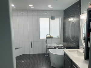 Bathroom featuring a stall shower, a soaking tub, tile walls, and vanity