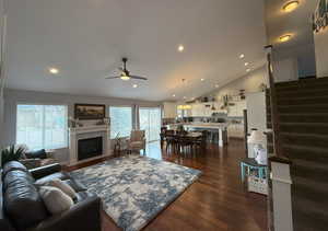 Living room featuring ceiling fan, dark wood-style flooring, a fireplace with flush hearth, stairs, and vaulted ceiling