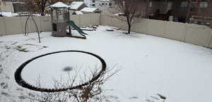 Yard covered in snow with a playground and fence