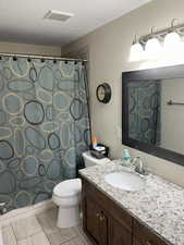 Full bathroom featuring visible vents, a shower with shower curtain, toilet, a textured ceiling, and vanity