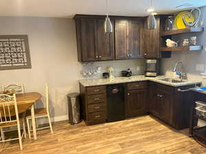 Kitchen with a sink, dark brown cabinets, light stone countertops, light wood finished floors, and decorative light fixtures