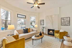 Living room with light wood-style floors, ceiling fan, baseboards, and a high end fireplace