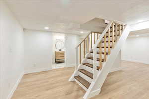 Staircase with a textured ceiling, recessed lighting, wood finished floors, and baseboards