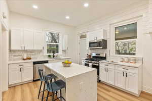 Kitchen with stainless steel appliances, a kitchen island, a sink, light wood-style floors, and white cabinets