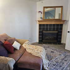 Living area with baseboards, dark colored carpet, and a tile fireplace