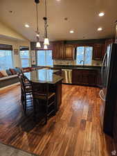 Kitchen with dark stone counters, a kitchen island, appliances with stainless steel finishes, dark wood-type flooring, and a sink