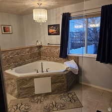 Full bath with a textured ceiling, tile patterned flooring, a bath, and baseboards