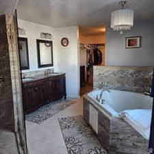 Full bathroom featuring a textured ceiling, tile patterned flooring, a sink, a bath, and double vanity