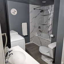 Full bath featuring a combined bath / shower with marble appearance, a sink, wood finished floors, baseboards, and washing machine and clothes dryer