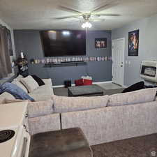 Carpeted living area with a textured ceiling, ceiling fan, baseboards, and heating unit