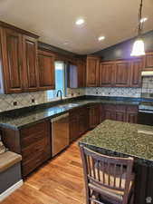 Kitchen featuring appliances with stainless steel finishes, vaulted ceiling, a sink, light wood-type flooring, and under cabinet range hood