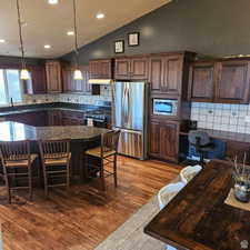 Kitchen featuring lofted ceiling, a kitchen breakfast bar, appliances with stainless steel finishes, a center island, and dark countertops