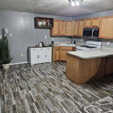 Kitchen featuring white range with gas stovetop, stainless steel microwave, a peninsula, light countertops, and open shelves