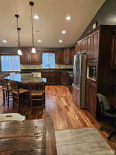 Kitchen featuring stainless steel appliances, a sink, hanging light fixtures, decorative backsplash, and dark wood finished floors