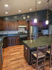 Kitchen with stainless steel appliances, under cabinet range hood, a kitchen bar, and a center island