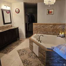 Bathroom with double vanity, a sink, a textured ceiling, tile patterned flooring, and a bath