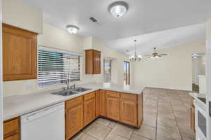 Kitchen with a peninsula, white dishwasher, light countertops, and a sink