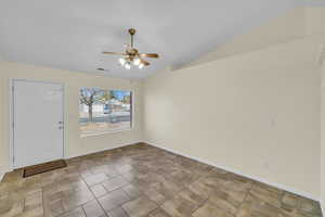 Empty room with vaulted ceiling, ceiling fan, visible vents, and baseboards