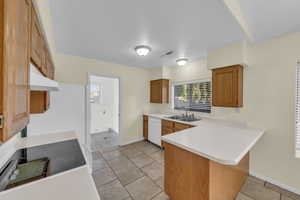 Kitchen with a peninsula, a sink, light countertops, dishwasher, and brown cabinetry