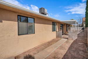 Entrance to property featuring central AC unit, fence, and stucco siding