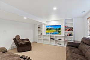 Carpeted living room featuring baseboards, built in shelves, visible vents, and recessed lighting