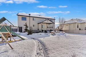 Snow covered rear of property with a playground, fence, and stucco siding