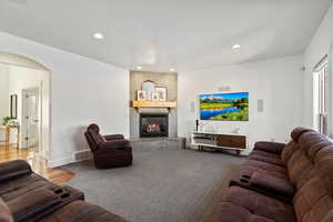 Carpeted living area featuring arched walkways, recessed lighting, a large fireplace, visible vents, and baseboards