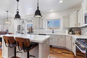 Kitchen with stainless steel appliances, white cabinetry, light countertops, a center island, and decorative light fixtures