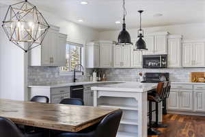 Kitchen featuring black appliances, hanging light fixtures, white cabinetry, and a center island