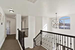 Hall featuring visible vents, dark carpet, an upstairs landing, and a notable chandelier