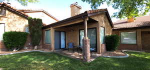 Back of house with a tiled roof, brick siding, a lawn, and a chimney