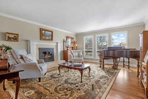 Living room with baseboards, light wood finished floors, a tiled fireplace, and crown molding