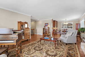 Living room with wood finished floors, visible vents, baseboards, ornamental molding, and an inviting chandelier