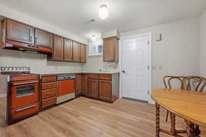 Kitchen with light countertops, visible vents, light wood-style flooring, range, and dishwasher