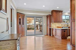 Kitchen featuring crown molding, light countertops, light wood-style flooring, glass insert cabinets, and brown cabinetry