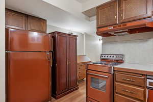 Kitchen featuring under cabinet range hood, light wood-style floors, light countertops, range, and freestanding refrigerator