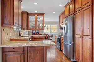 Kitchen with light stone counters, a peninsula, a sink, appliances with stainless steel finishes, and glass insert cabinets